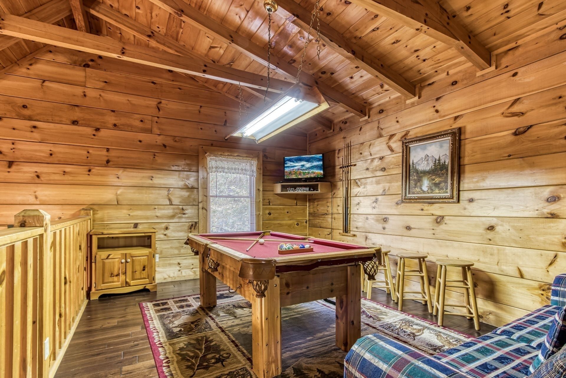 A cozy wooden cabin interior with a pool table, a television, and a painting on the wall.