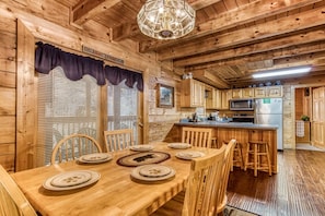 A wooden cabin interior with a dining area, kitchen, and a chandelier.
