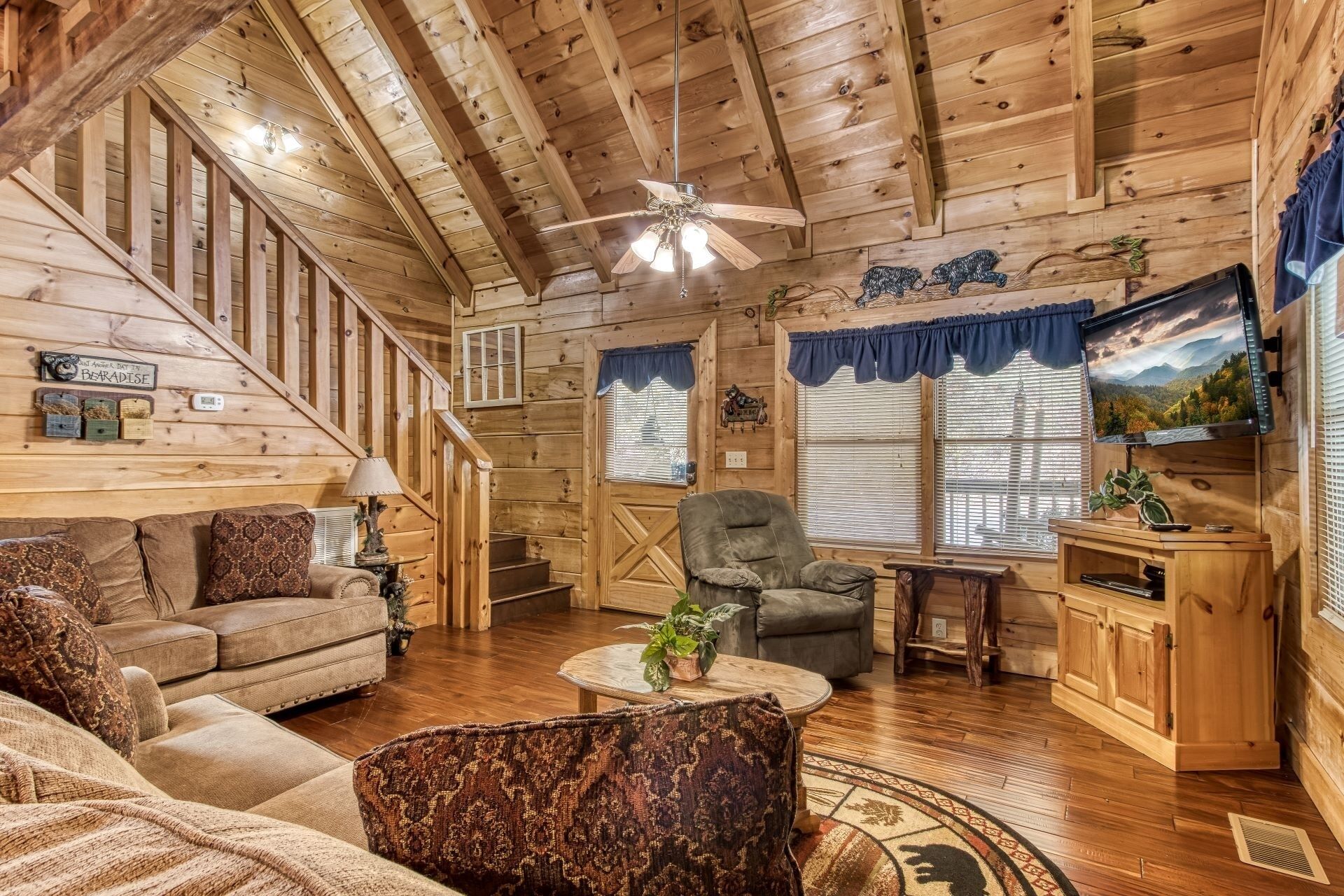 A cozy cabin interior with a wooden staircase, a sofa, a chair, a coffee table, and a television.