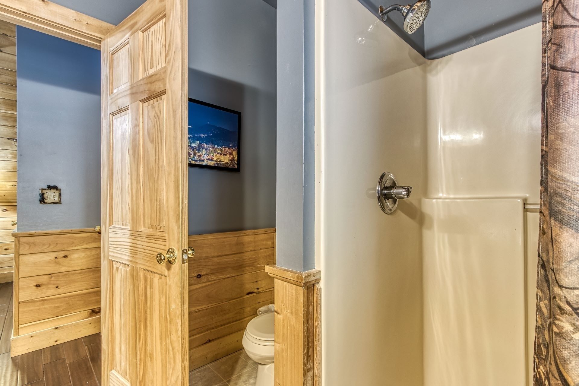 A bathroom with wooden paneling, a toilet, a shower with a glass door, and a framed picture on the wall.