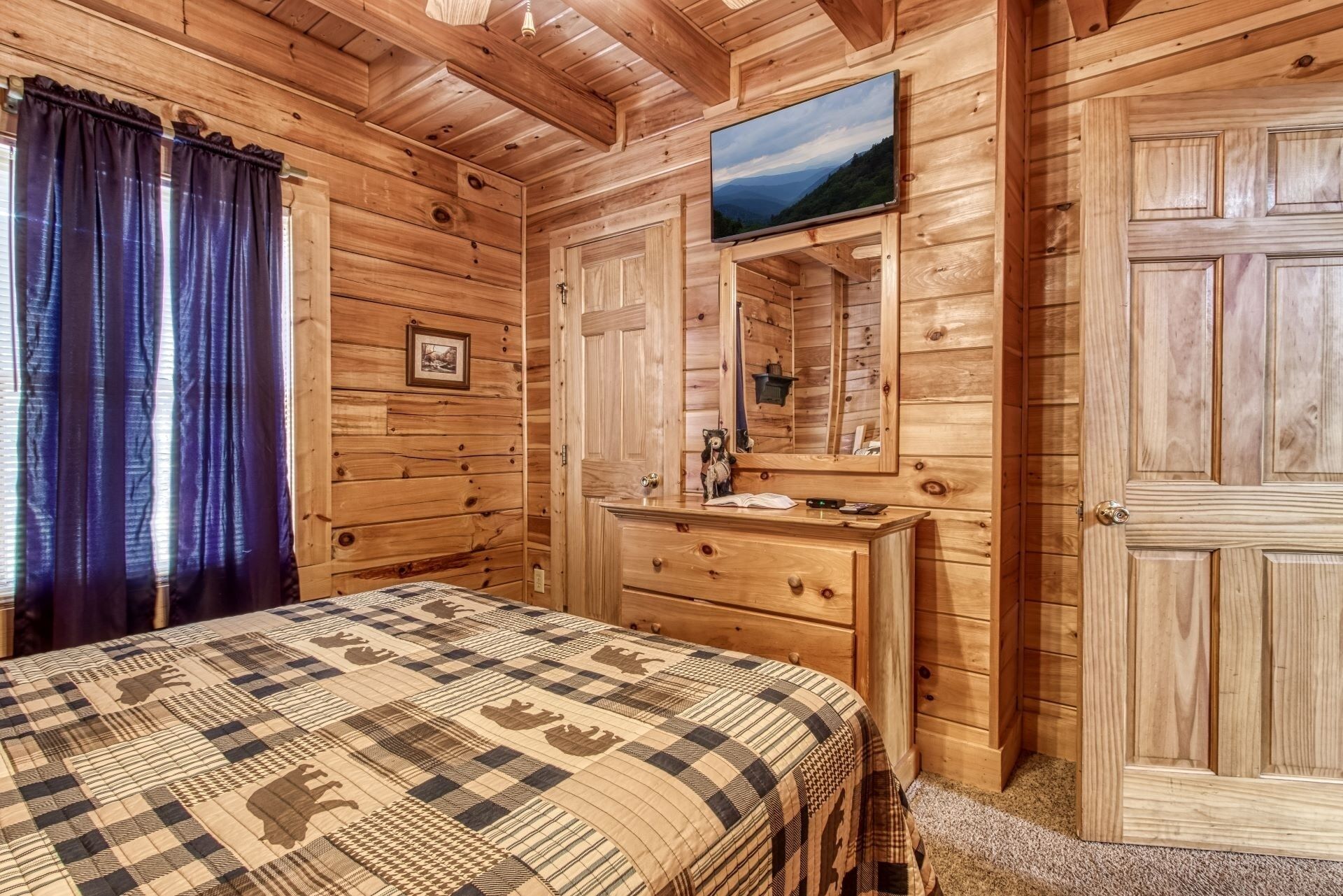 A wooden cabin bedroom with a bed, dresser, and a mounted TV.