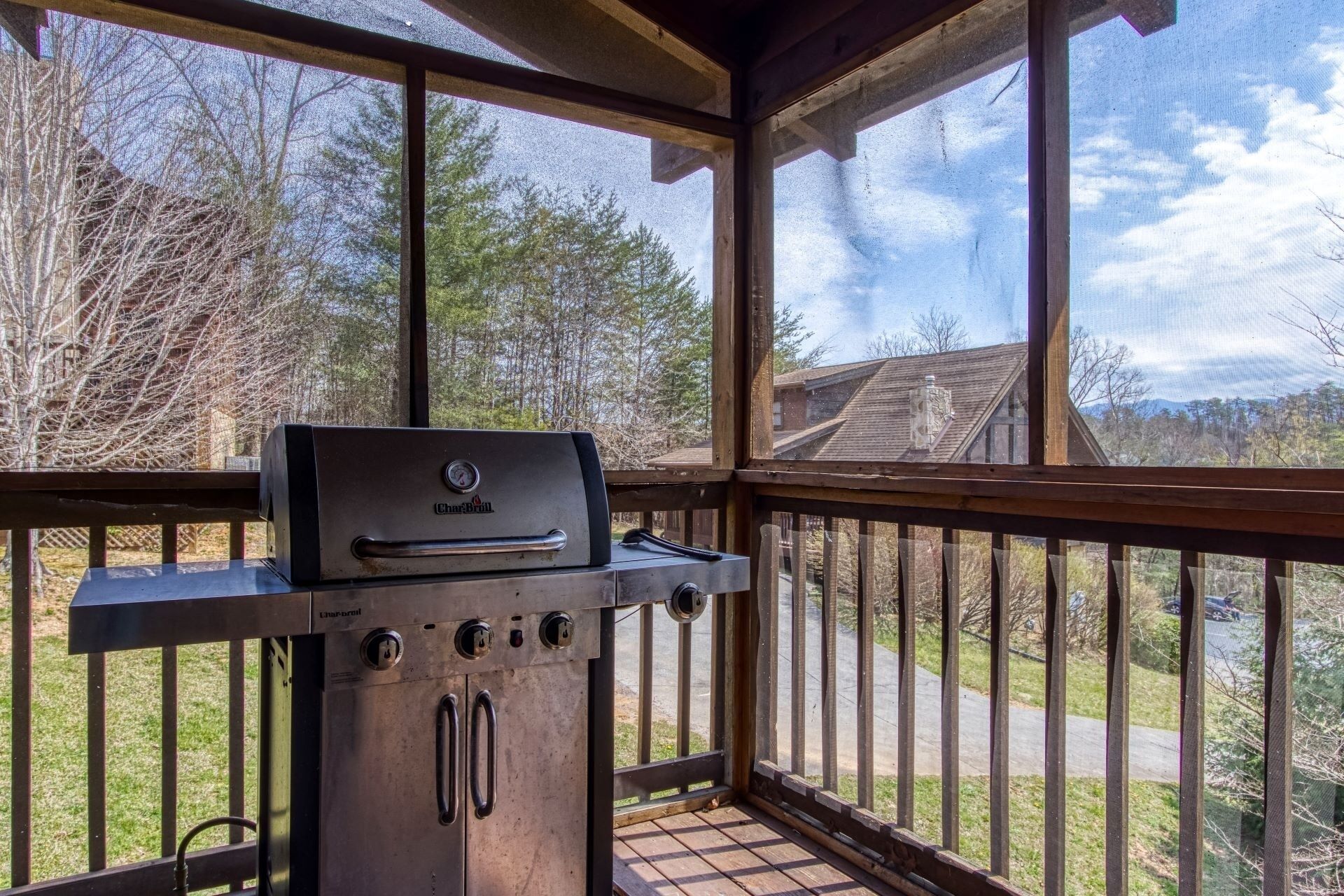 A barbecue grill on a wooden deck with a view of a house and trees.