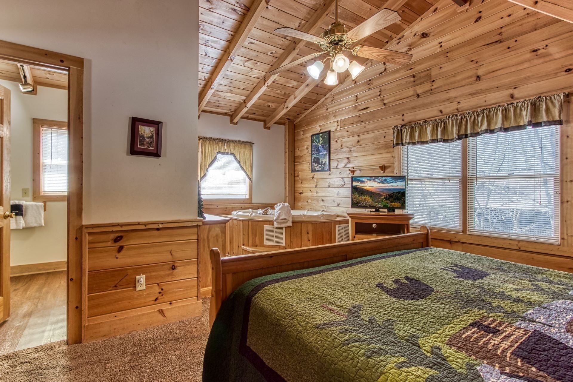 Quarto de cabana de madeira com cama, escrivaninha, televisão e ventilador de teto.