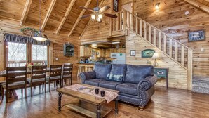 A cozy cabin interior with a dining area, a living room with a sofa and coffee table, a kitchen, and a staircase. - Er6 - On Eagles' Wings - Great Location. Close To All The Action! 6 Bedroom Cabin by RedAwning (Pigeon Forge)