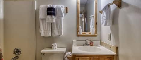 A bathroom with a toilet, sink, and bathtub. There are towels hanging on a rack and a mirror above the sink.