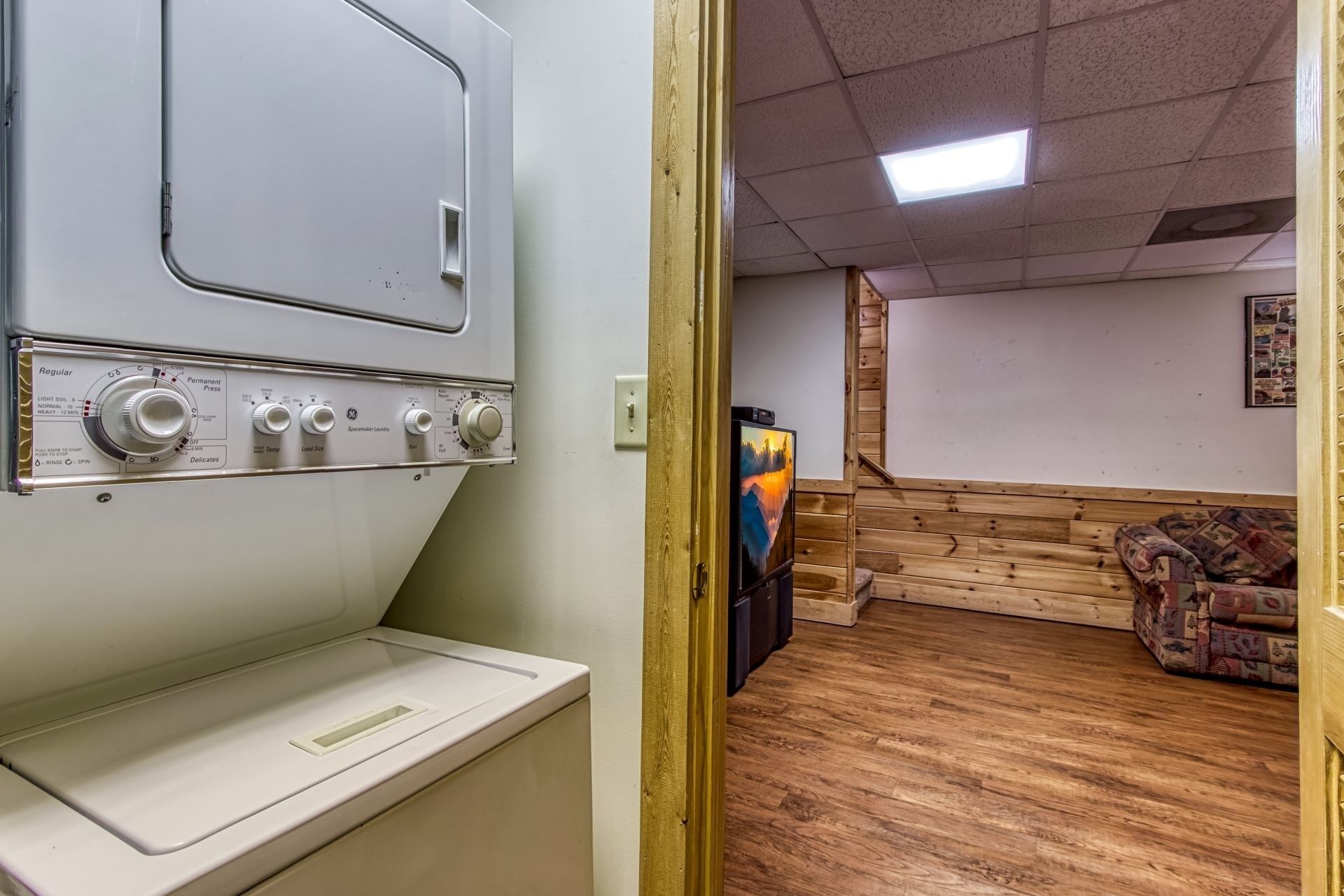 A laundry room with a washing machine, a dryer, and a wooden staircase leading to a living area with a television.