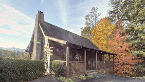 A log cabin with a stone chimney, wooden porch, and a view of autumn foliage. - Er6 - On Eagles' Wings - Great Location. Close To All The Action! 6 Bedroom Cabin by RedAwning (Pigeon Forge)