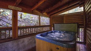 A wooden cabin with a hot tub, a 'No Smoking' sign, and a view of the forest through the windows.