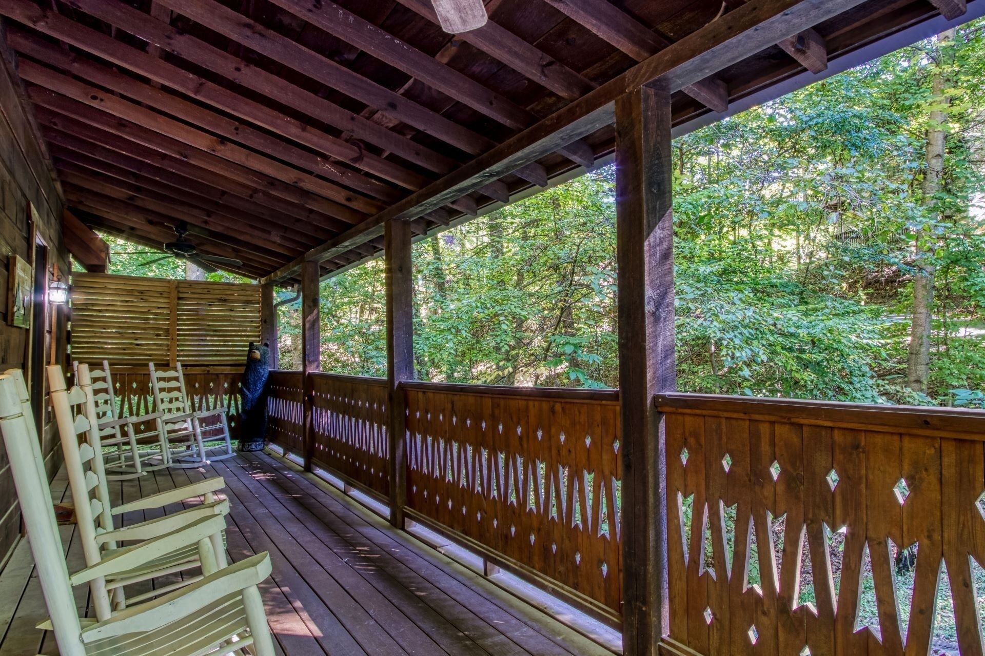 A covered wooden deck with benches, a wooden railing, and a view of a forested area.