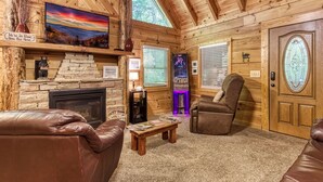 A cozy cabin interior with a stone fireplace, leather furniture, a mounted TV, and a wooden door with a stained glass window. - Er96 - Squirrel's Leap - Great Location! Close To Town! 2 Bedroom Cabin by RedAwning (Pigeon Forge)