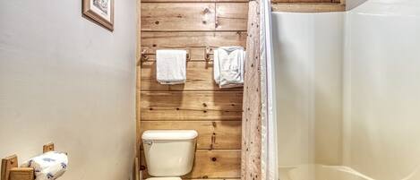 Un baño con pared de madera, un inodoro, una ducha y un cuadro enmarcado.