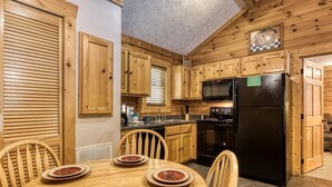 Cocina de estilo cabaña de madera con una mesa de comedor para cuatro personas, un refrigerador negro y armarios de madera.