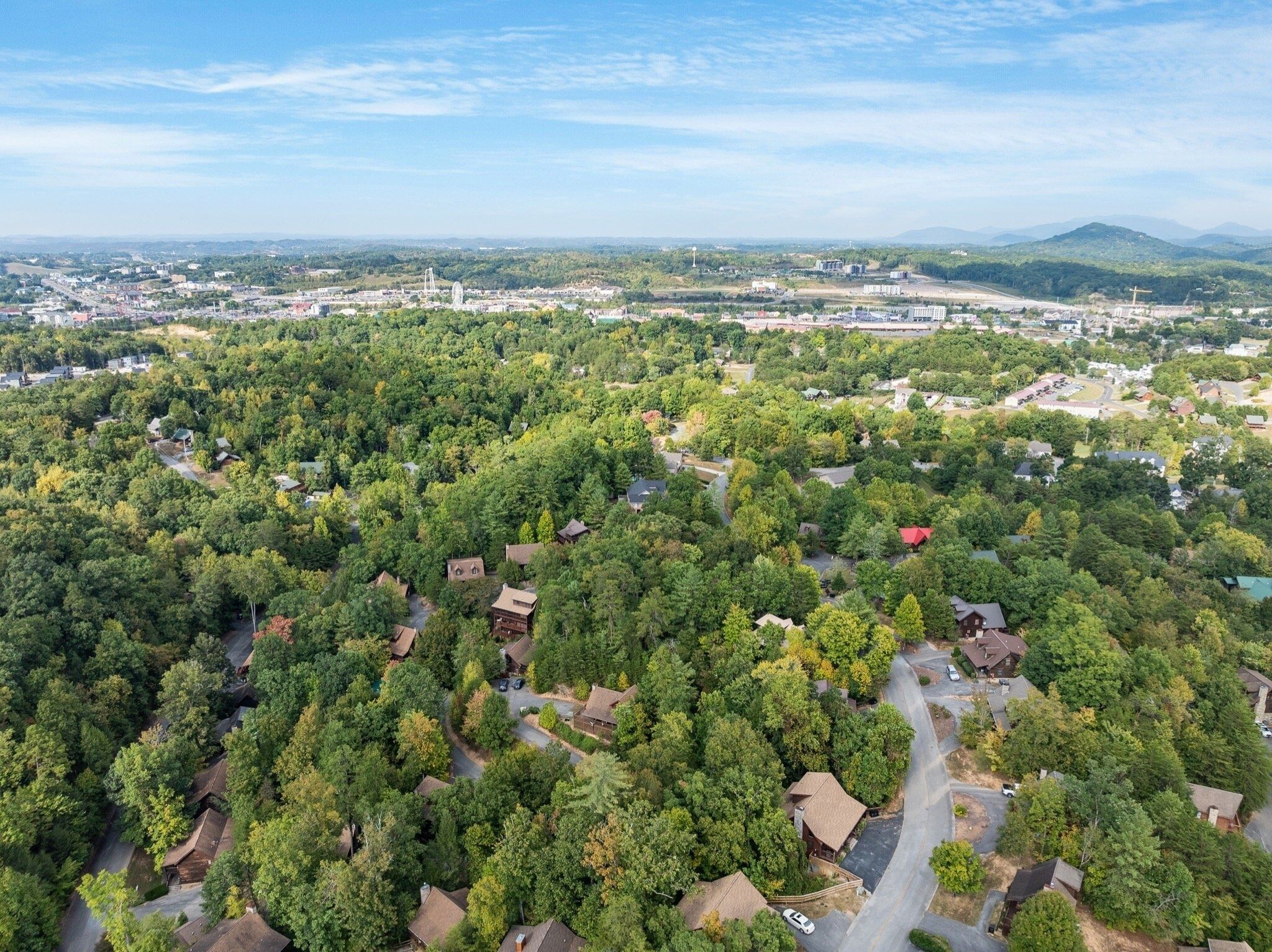 Una vista aerea di una zona residenziale con case immerse nel verde, un cielo sereno e montagne sullo sfondo.