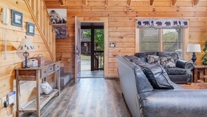 A log cabin interior with a wooden floor, a leather sofa, a wooden table, and a door leading outside.