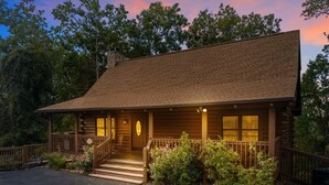 A rustic log cabin with a porch, steps, and a chimney.