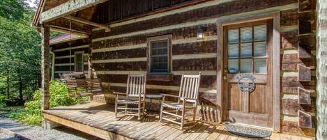 A rustic log cabin with a porch, two rocking chairs, and a welcome sign.