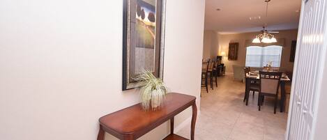 A hallway with a wooden console table, a framed picture, and a dining area with chairs and a table.
