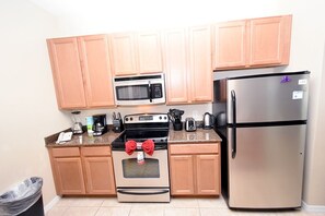 A kitchen with wooden cabinets, a stainless steel refrigerator, a microwave, a stove, and a trash bin. - Paradise Palms -5 Bed Townhome W-splashpool-3046pp 5 Bedroom Townhouse by RedAwning (Kissimmee)