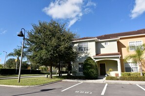 A two-story building with a flat roof, a parking lot with marked spaces, and a street lamp. - Paradise Palms -5 Bed Townhome W-splashpool-3046pp 5 Bedroom Townhouse by RedAwning (Kissimmee)