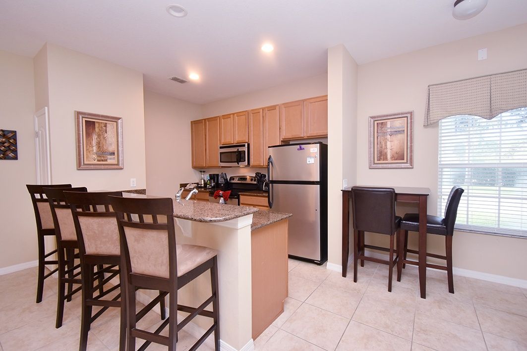 A kitchen with wooden cabinets, a stainless steel refrigerator, a microwave, and a dining area with chairs and a table.