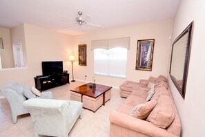 Ein Wohnzimmer mit Sofa, Sessel, Couchtisch, Fernseher und Deckenventilator.