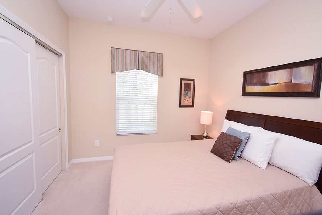 A bedroom with a bed, a nightstand, a window with blinds, a door, and a painting on the wall.
