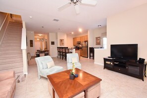 A living room with a wooden coffee table, a television on a stand, a staircase, and a kitchen in the background. - Paradise Palms -5 Bed Townhome W-splashpool-3046pp 5 Bedroom Townhouse by RedAwning (Kissimmee)