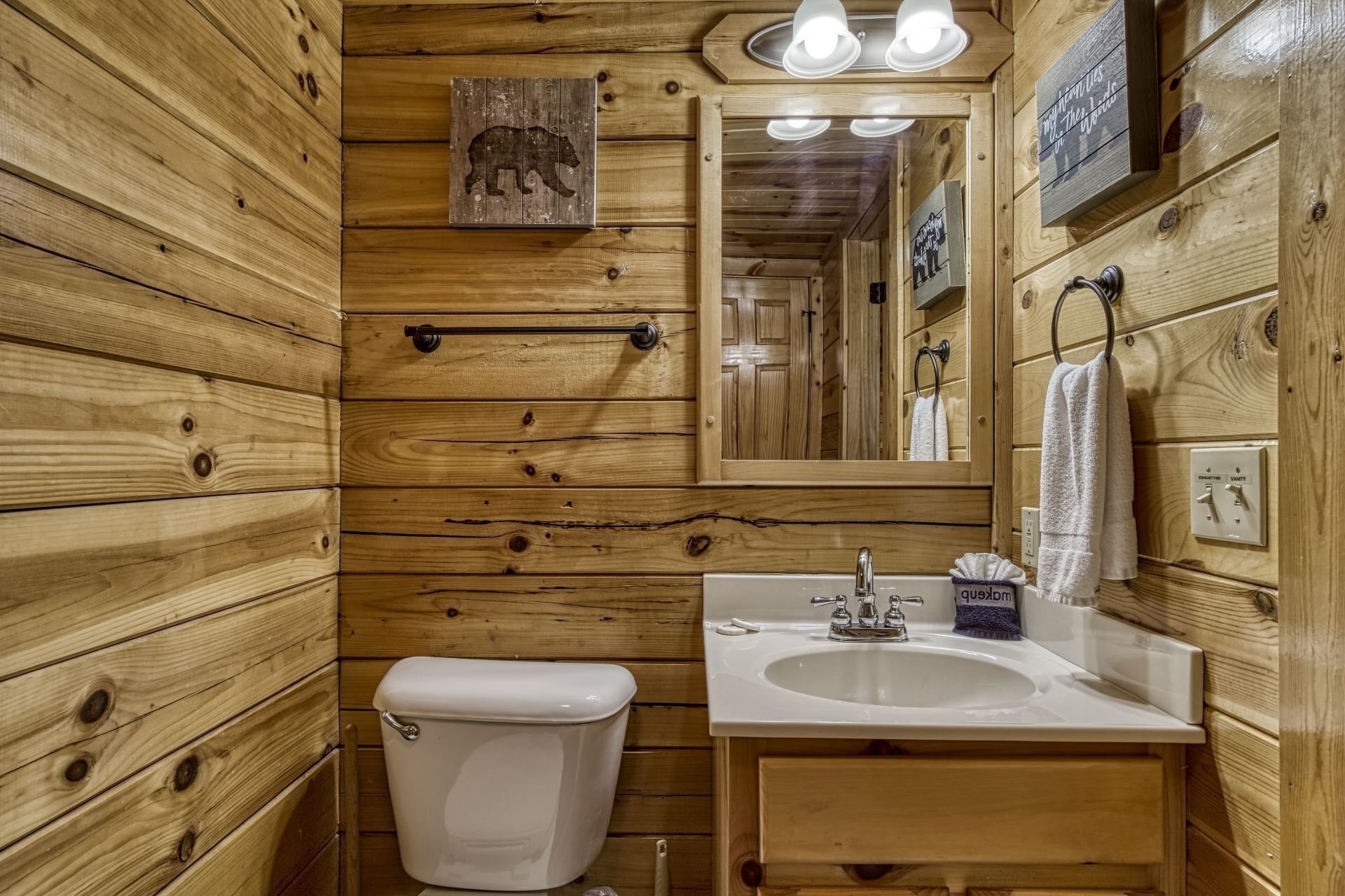 Une salle de bain rustique, aménagée dans une cabane en bois, avec des toilettes, un lavabo et un miroir.