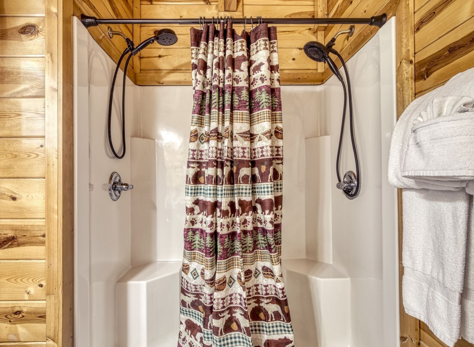 A shower with a patterned curtain, wooden walls, and a towel rack.