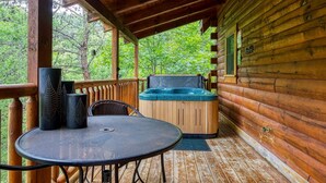 Eine Holzhütte mit einer Veranda, einem runden Tisch mit Stühlen und einem Whirlpool.