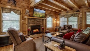 Ein gemütliches Blockhaus-Interieur mit Kamin aus Stein, Holzwänden und einem großen Fenster mit Blick auf eine schöne Landschaft.