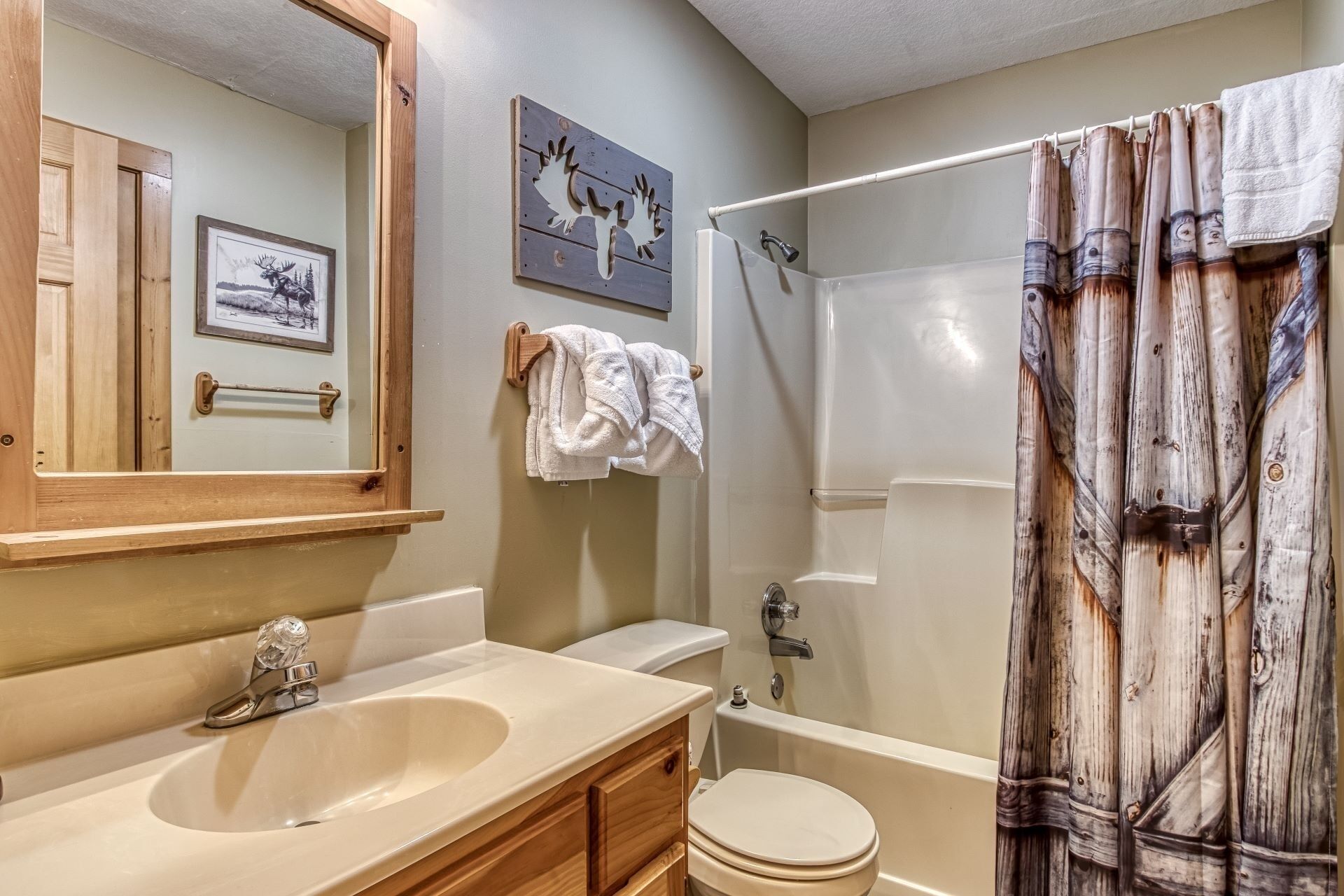 A bathroom with a sink, toilet, and shower. There is a towel rack with towels and a framed picture on the wall.
