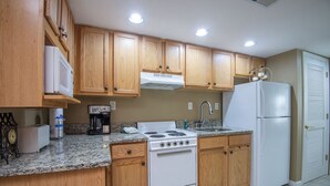 Una cocina con armarios de madera, estufa blanca, refrigerador y encimeras de granito.