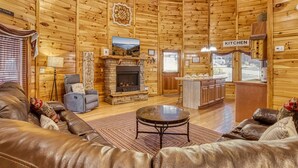 A cozy log cabin interior with a fireplace, a sofa, a dining area, and a kitchen. - Declan's View - Cozy 1 bedroom with Game room and Great Mountain Views! 1 Cabin by RedAwning (Sevierville)