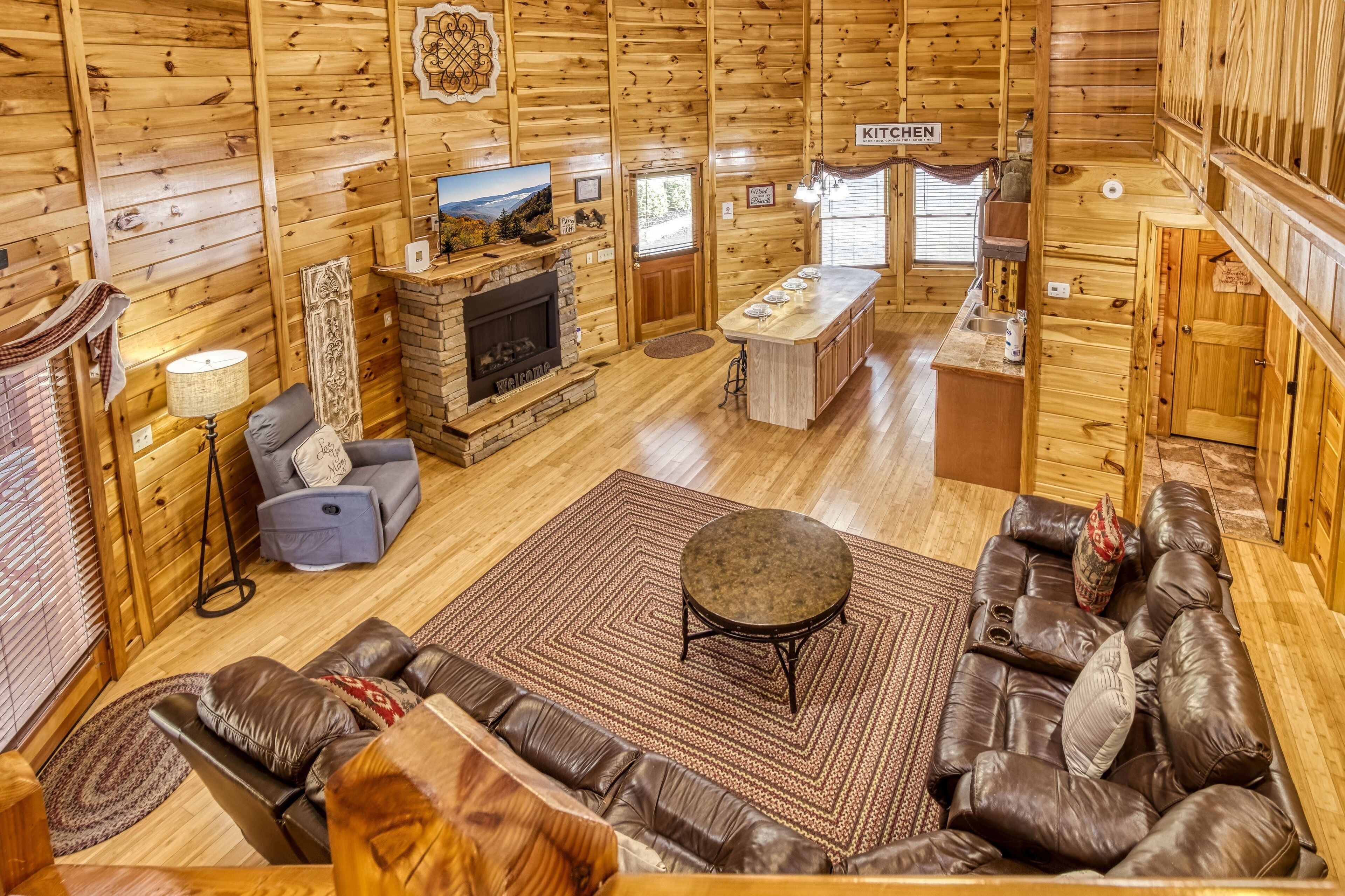A log cabin interior with a fireplace, sofa, and a kitchen area.