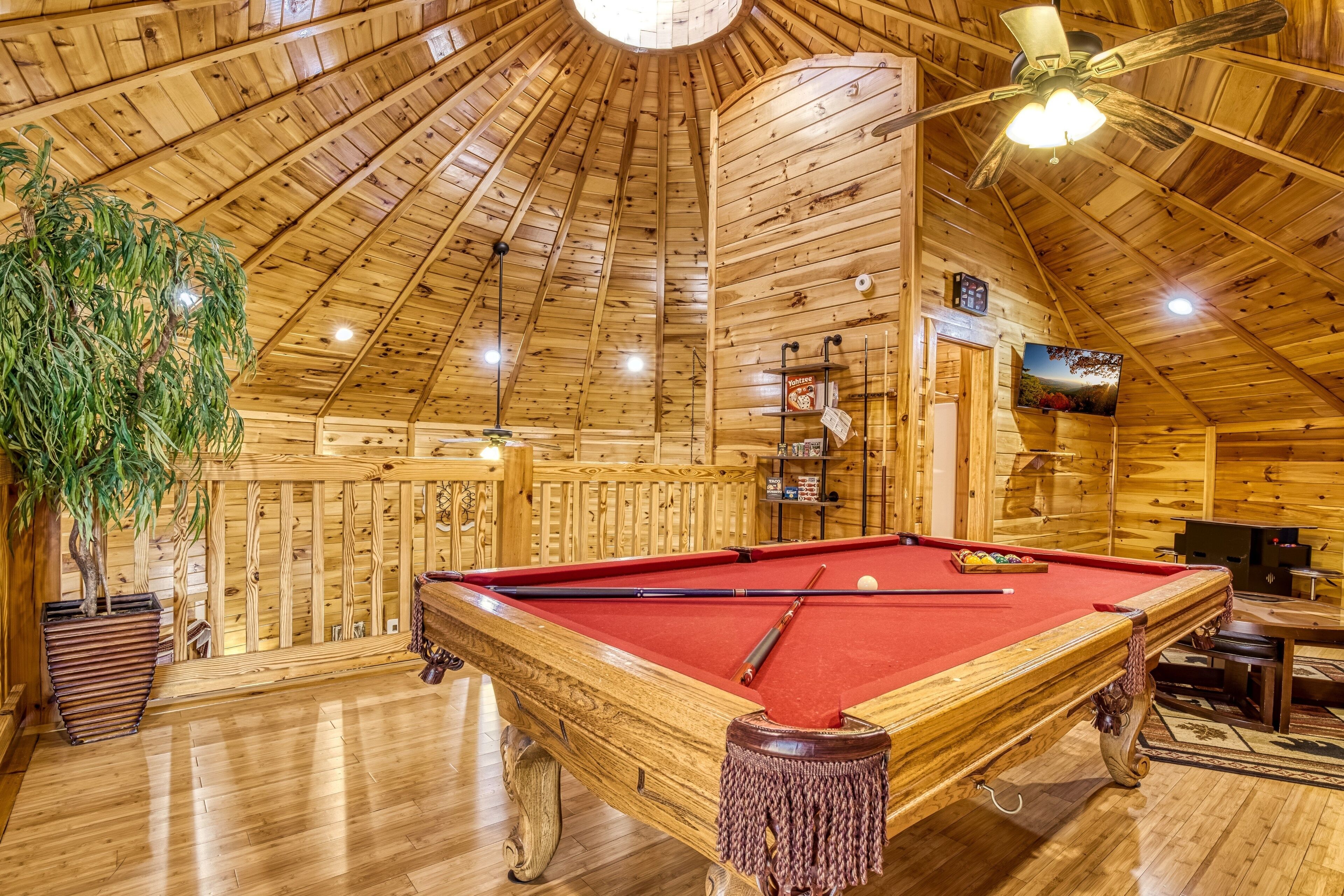 A wooden interior with a pool table, a ceiling fan, and a large plant.