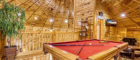 A wooden interior with a pool table, a ceiling fan, and a large plant.