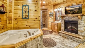 A wooden cabin interior with a large bathtub, stone fireplace, and wooden walls. - Declan's View - Cozy 1 bedroom with Game room and Great Mountain Views! 1 Cabin by RedAwning (Sevierville)