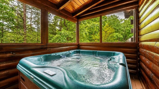 A hot tub in a log cabin with wooden walls and large windows overlooking a forest.