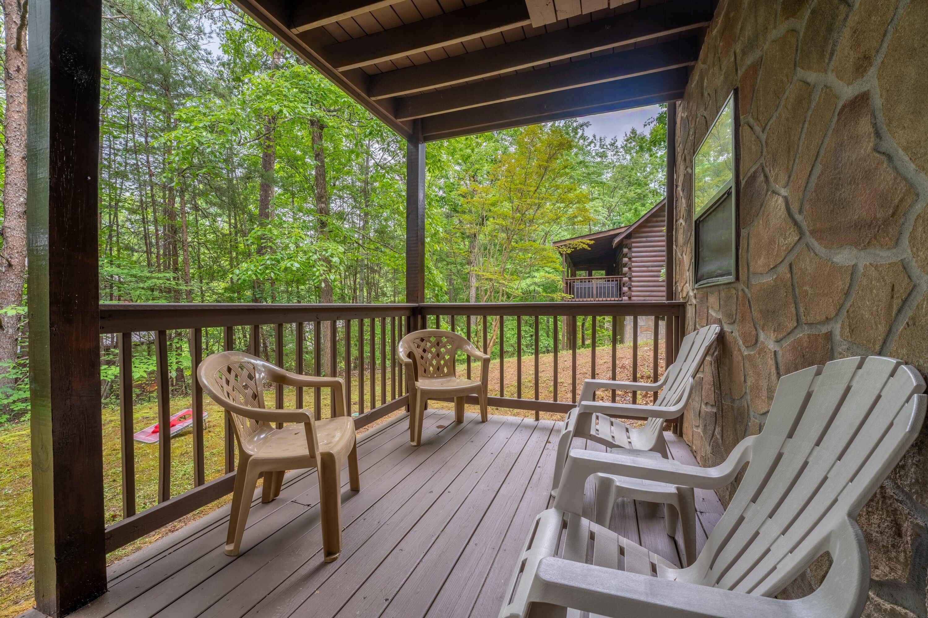 A covered porch with Adirondack chairs, a stone wall, and a view of a forest.