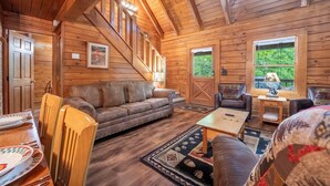 A wooden cabin interior with a sofa, chairs, a table, and a staircase.