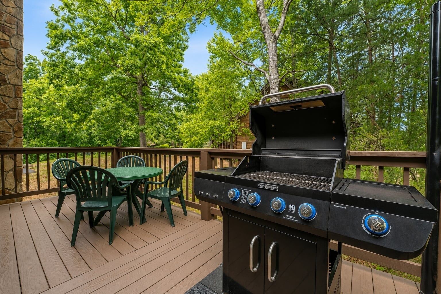 Un barbecue extérieur doté de quatre brûleurs, un mur en pierre et une terrasse en bois avec des chaises vertes.