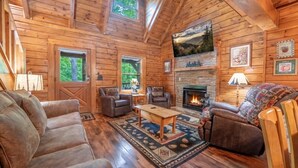 A log cabin interior with a fireplace, wooden walls, and a cozy seating area.
