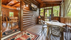 A log cabin with a dining area, a porch with chairs, and a view of the outdoors.