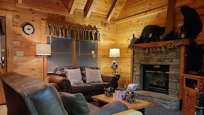 A cozy log cabin interior with a leather sofa, a wooden coffee table, a fireplace, and a clock on the wall. - ER246 - The Getaway Great Location - Close To Town! 2 Bedroom Cabin by RedAwning (Pigeon Forge)