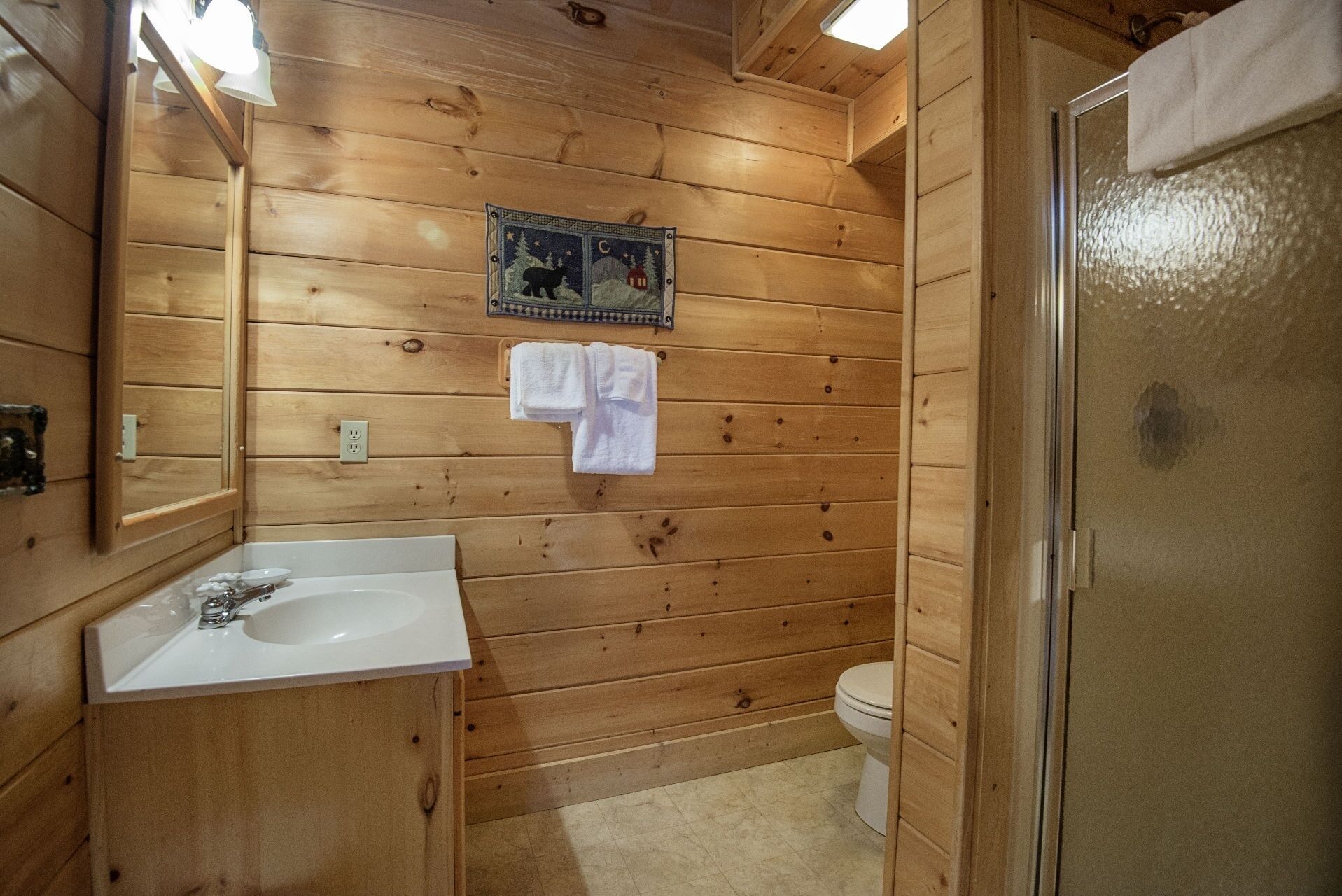 A wooden cabin bathroom with a sink, toilet, and a shower area.