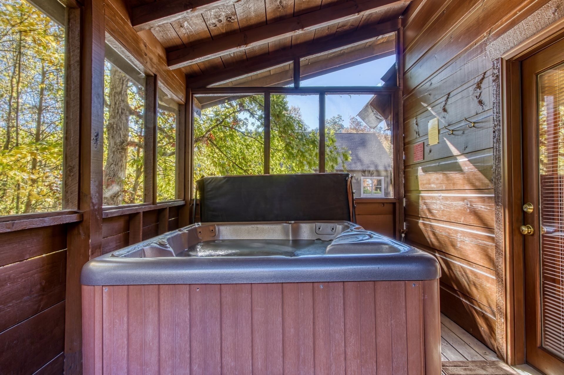 A wooden cabin with a hot tub in the center, large windows, and a door with a glass panel.