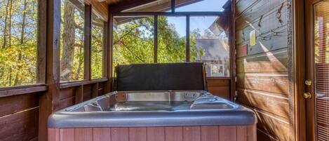 A wooden cabin with a hot tub in the center, large windows, and a door with a glass panel.
