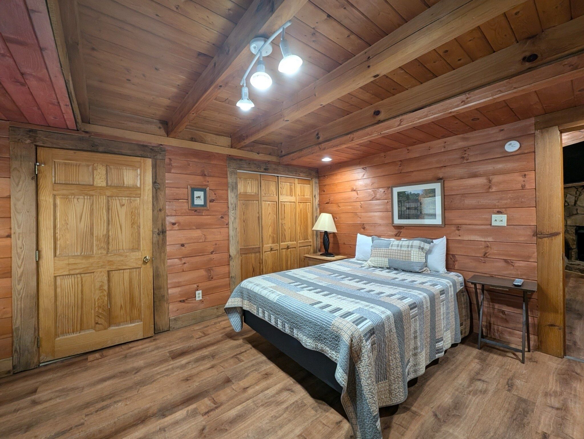 Ein Schlafzimmer einer Holzhütte mit einem Bett, einem Nachttisch und einer Wandlampe.