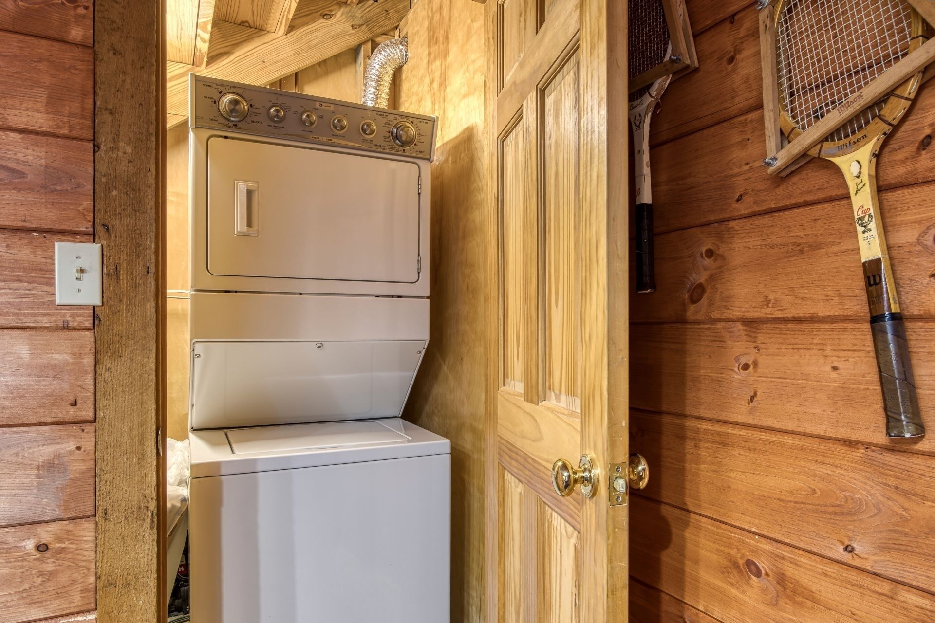 Un intérieur en bois avec un lave-linge et un sèche-linge blancs, une porte en bois et une raquette de tennis accrochée au mur.